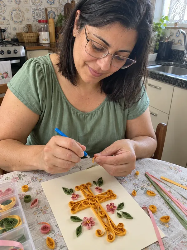 Cena ilustrativa: mulher praticando quilling em cruz decorativa
